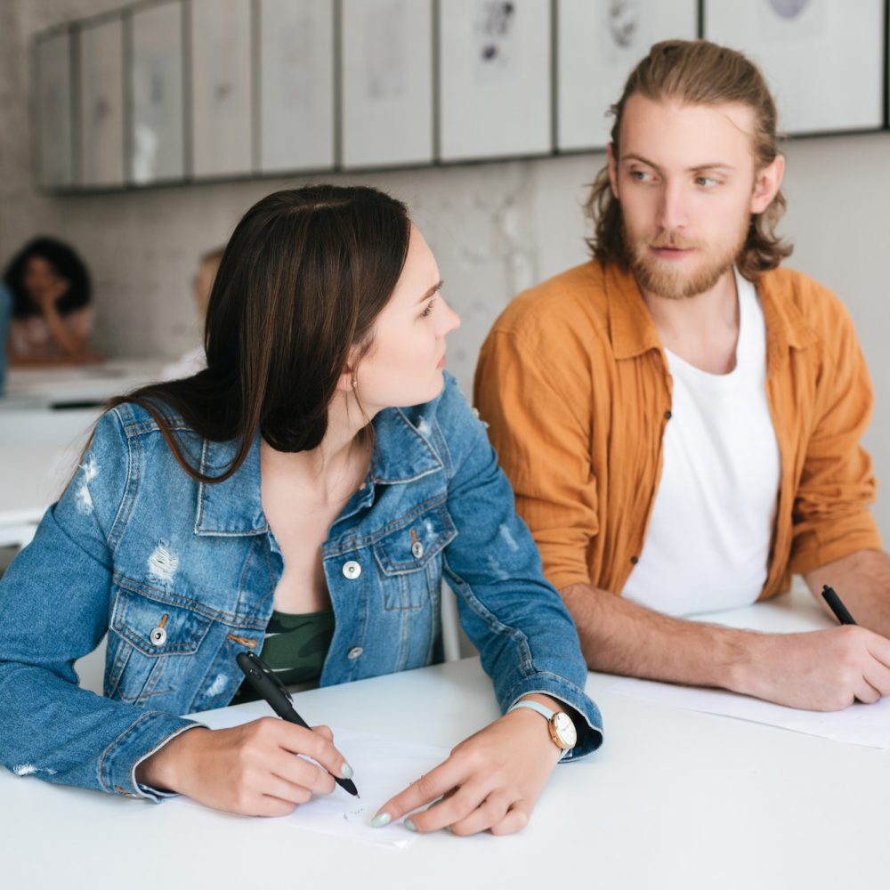 Two students sitting at the desk in classroom and thoughtfully looking on each other